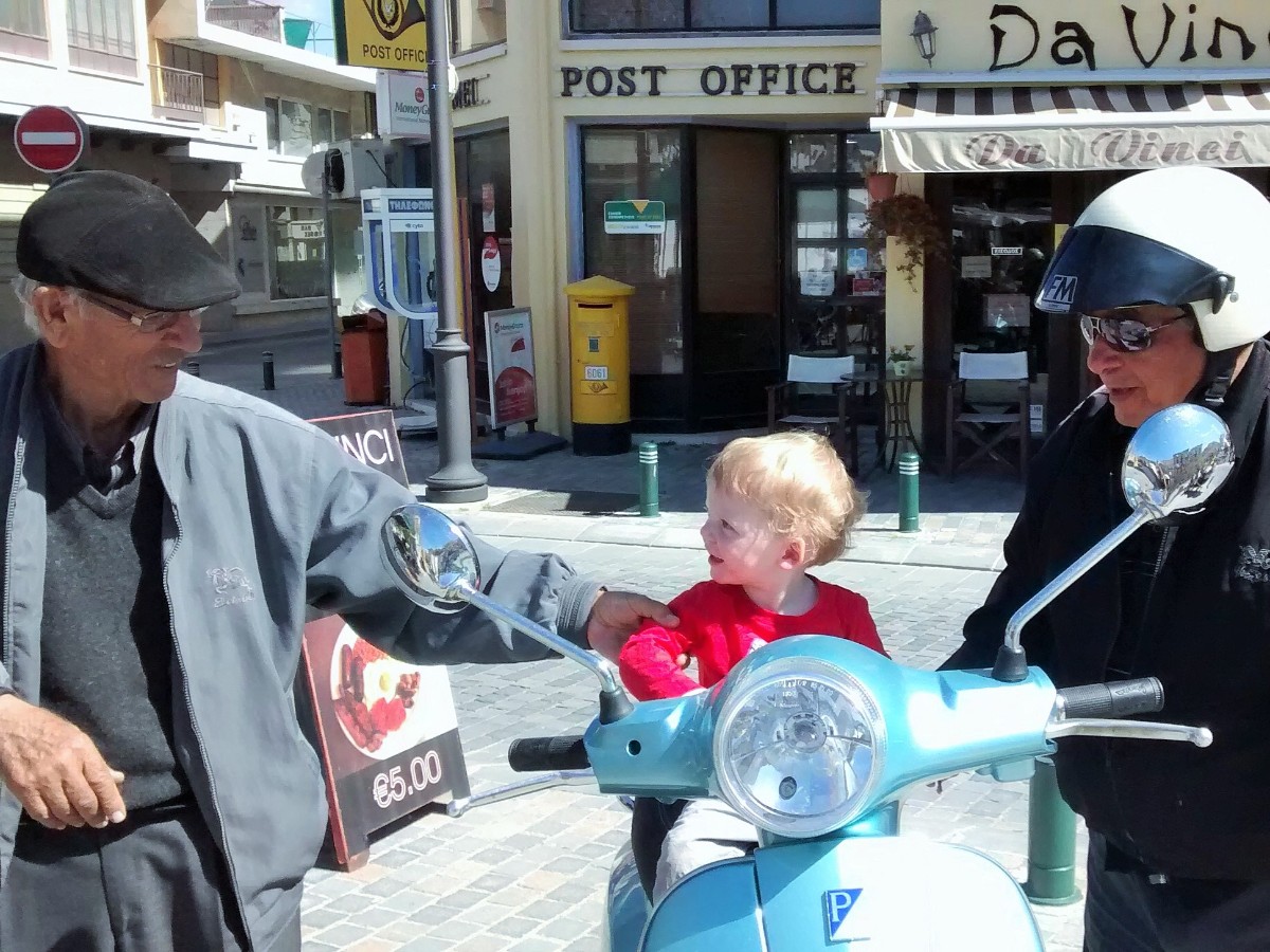 Toddler on scooter with old men in Larnaca, Cyprus