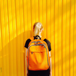 girl with yellow backpack next to yellow wall