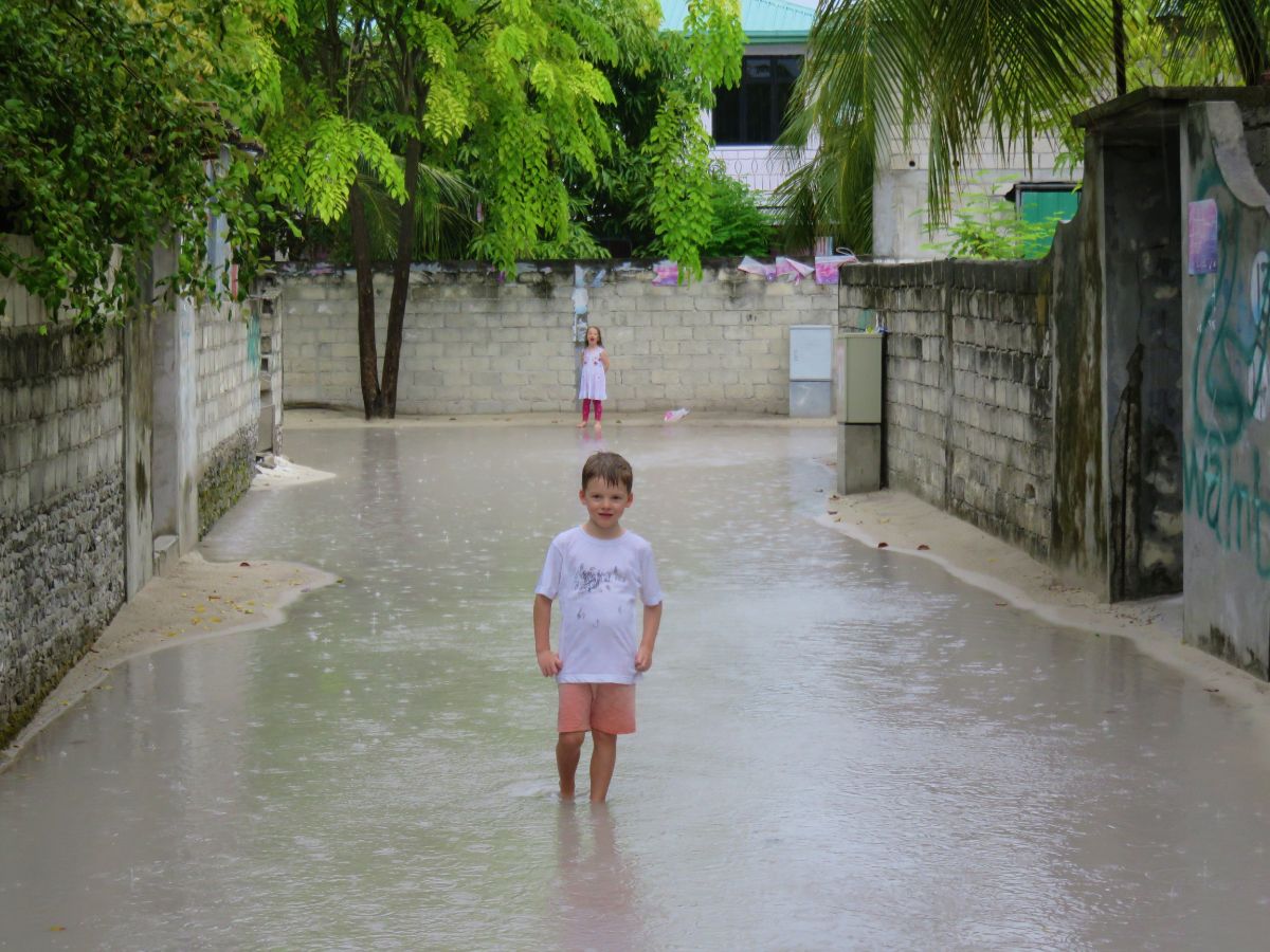 boy standing in puddle on road in Guraidhoo Island the Maldives