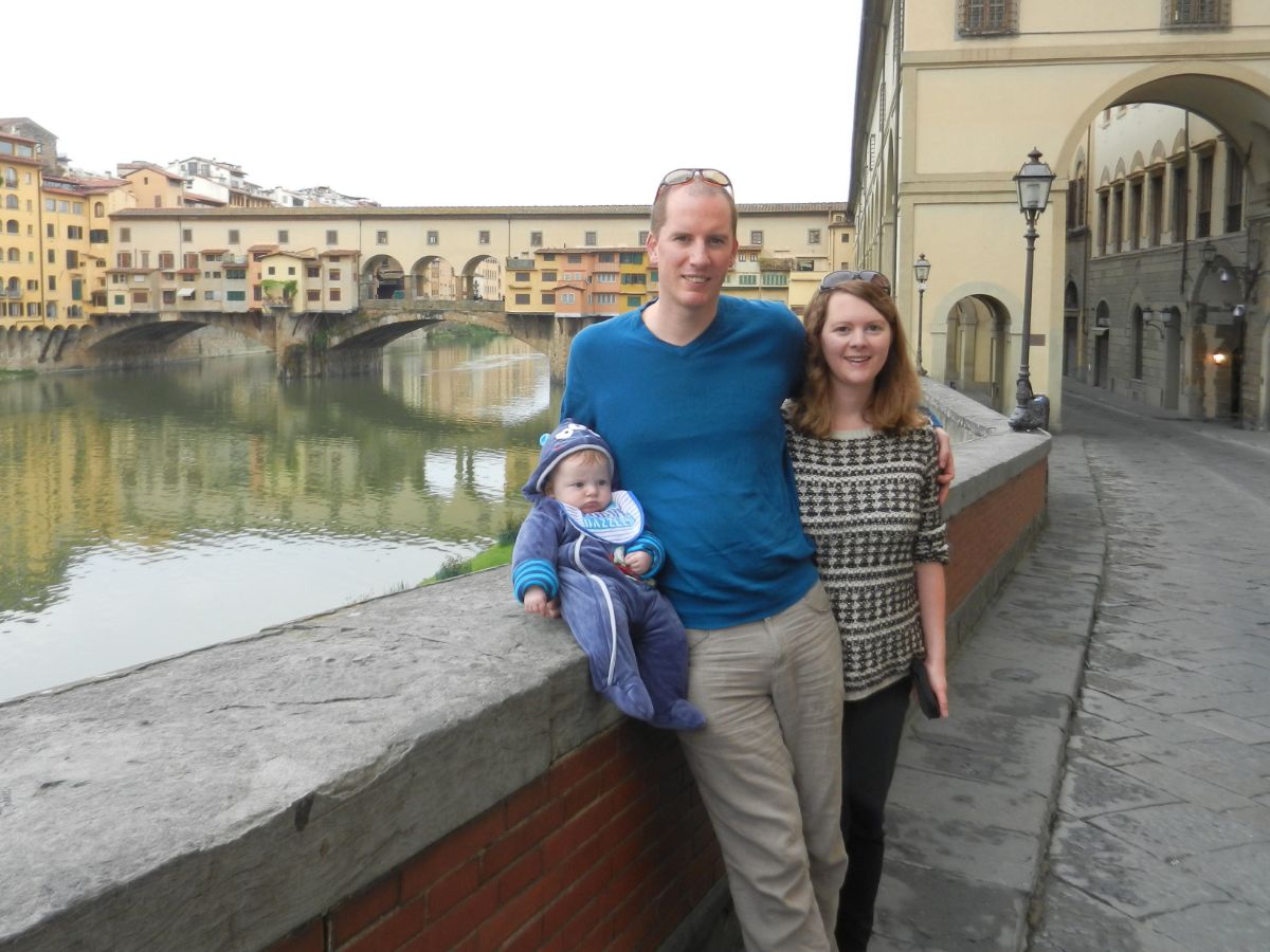 family with baby posing in front on Vecchio Bridge in Florence, Italy